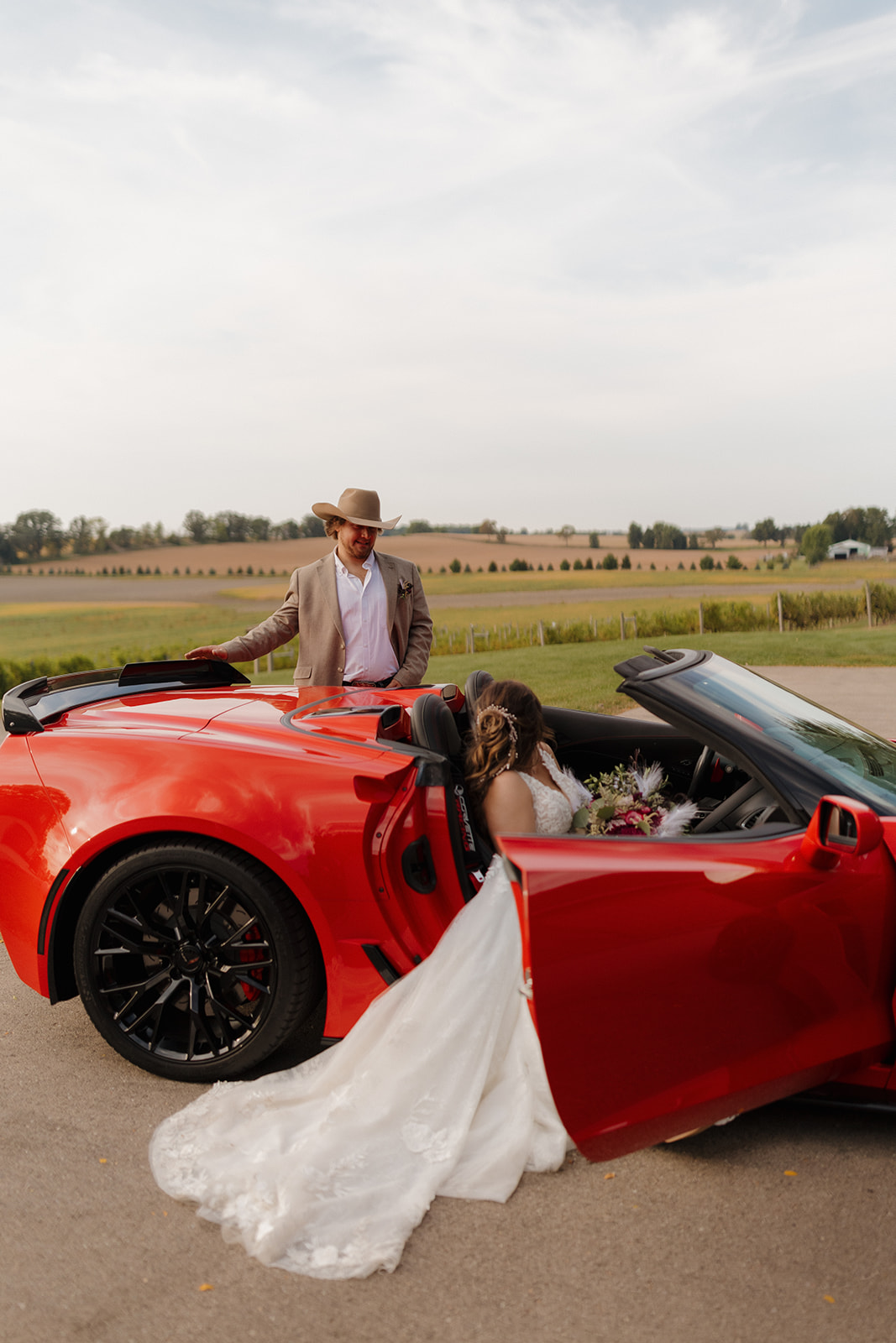 cowboy groom and bride pose with a red sports car on their wedding day in madison wisconsin