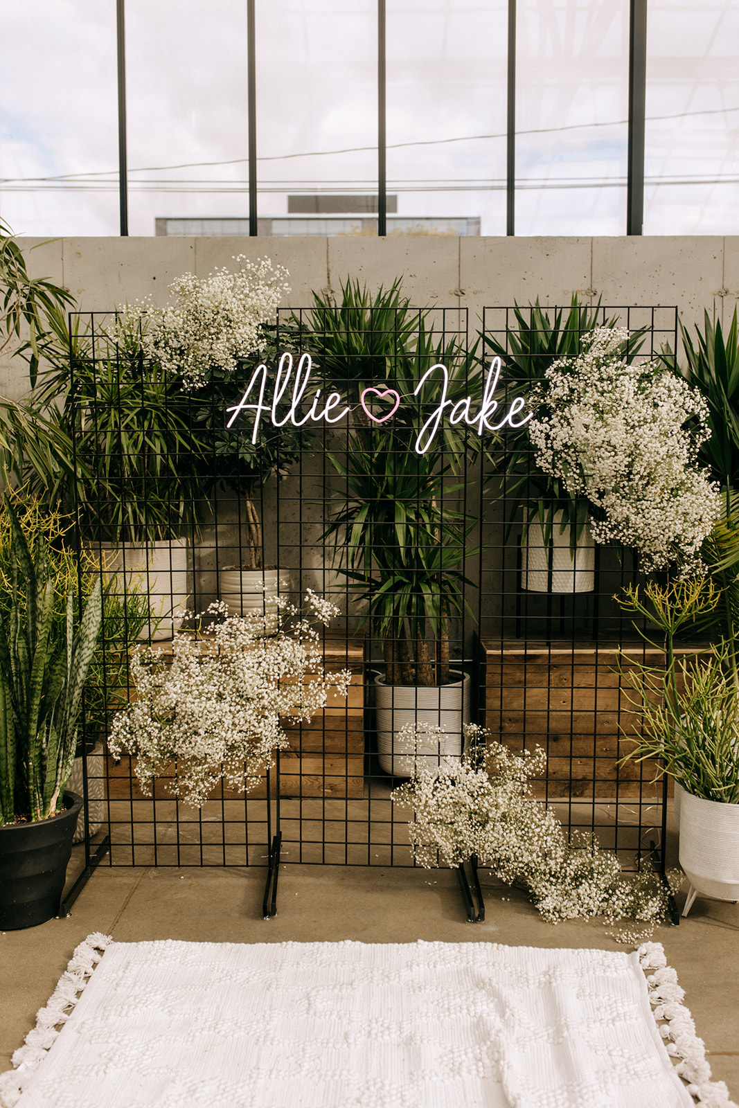 Modern wedding backdrop at The Tinsmith in Madison, Wisconsin with neon “Allie ❤️ Jake” sign, greenery, and baby’s breath accents