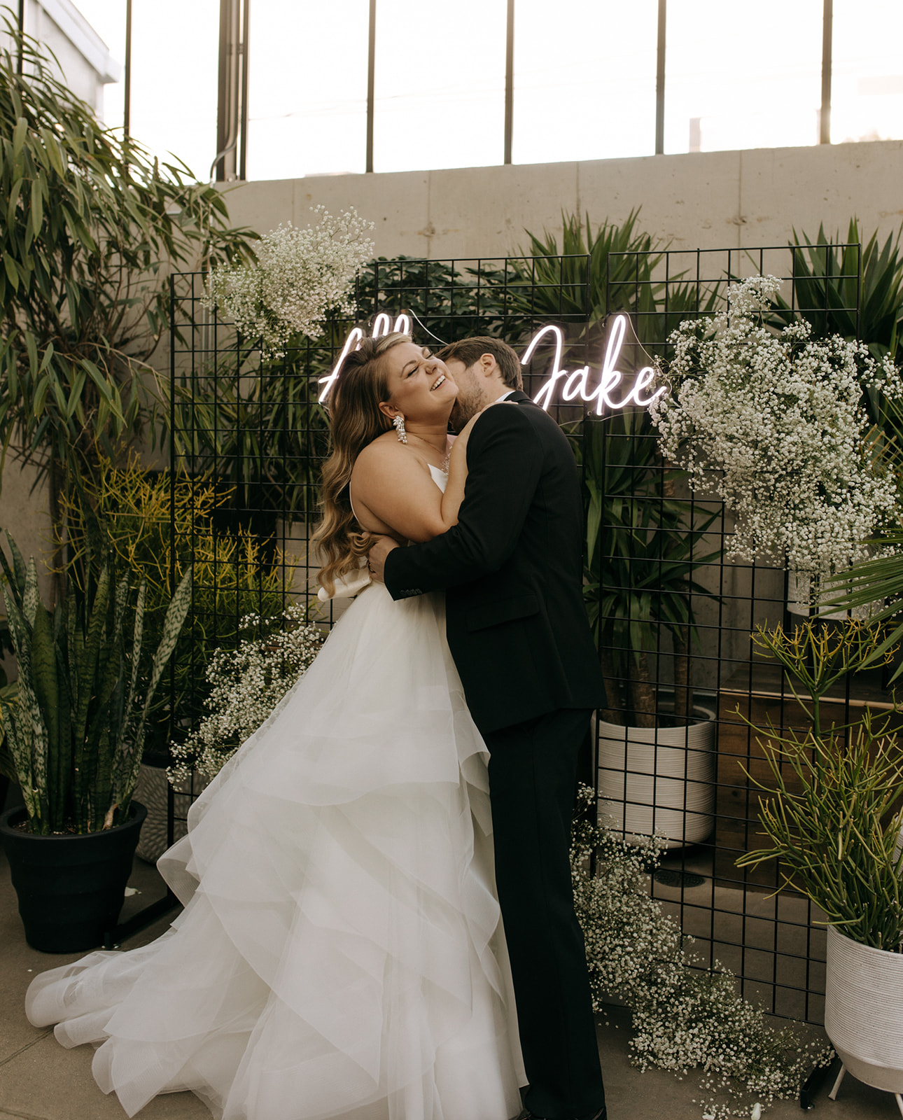 Couple sharing a playful moment under a neon sign at The Tinsmith, one of the top wedding venues in Madison