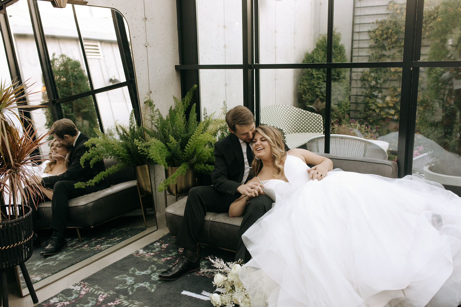 Couple cuddling in the lounge at The Tinsmith wedding venue in Madison, surrounded by greenery and glass walls
