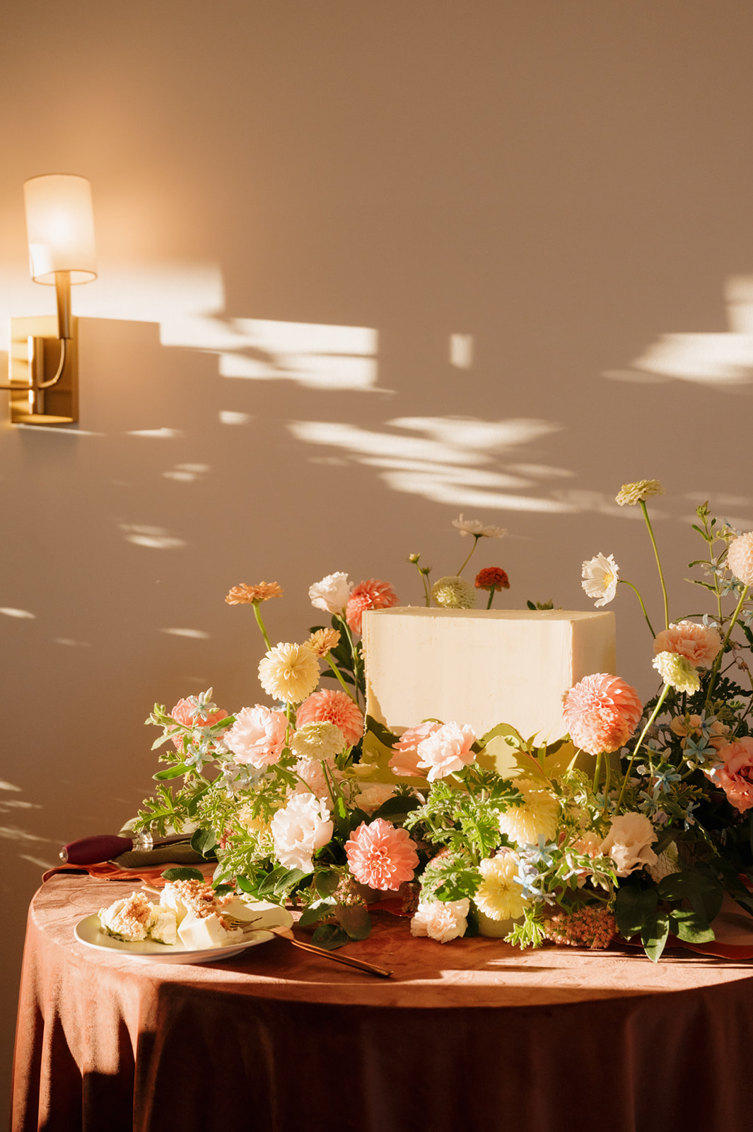 Minimalist wedding cake surrounded by pastel florals in golden sunlight at a luxury wedding venue in Madison, Wisconsin