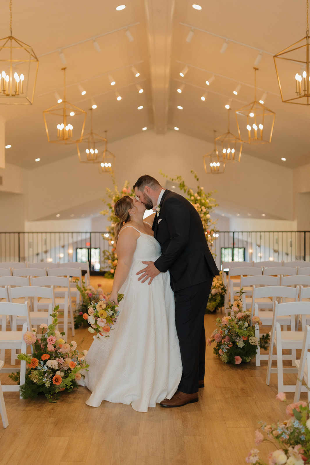 Newlyweds kissing inside The Eloise, one of the top wedding venues in Madison, surrounded by pastel florals and white chairs