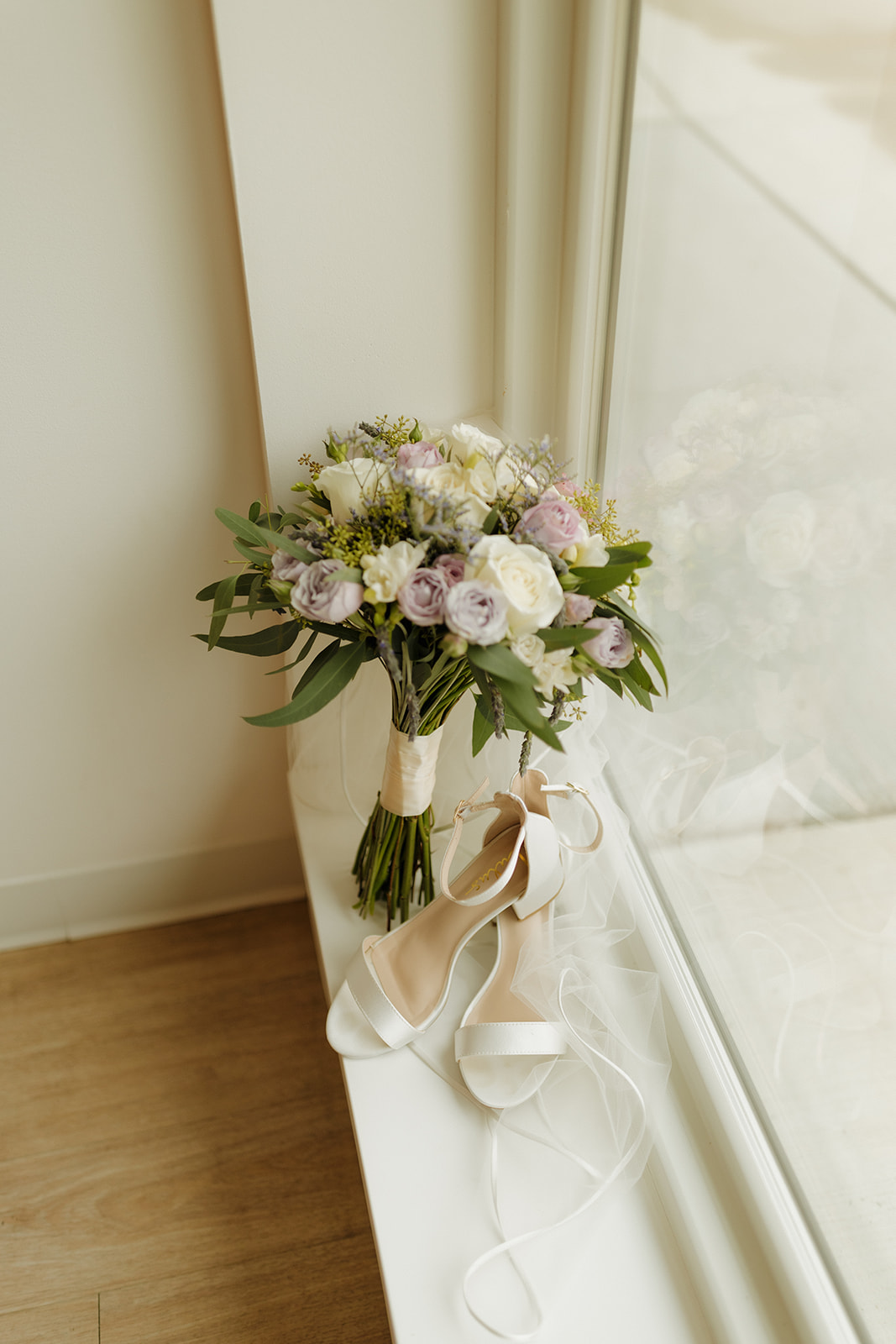 Bridal bouquet with blush and ivory roses next to wedding heels on a window ledge at The Eloise