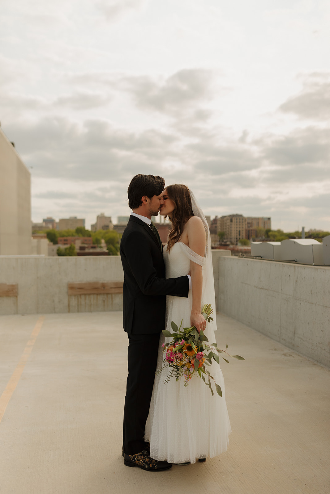 Bride and groom kiss on a Madison rooftop with city skyline in the background