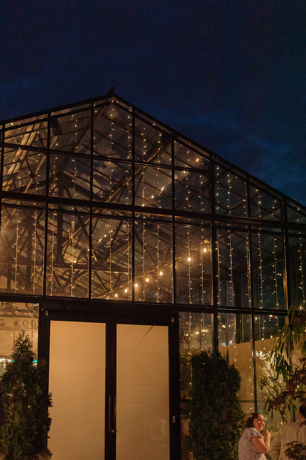 Exterior of The Tinsmith wedding venue in Madison at night, with twinkle lights glowing through glass atrium