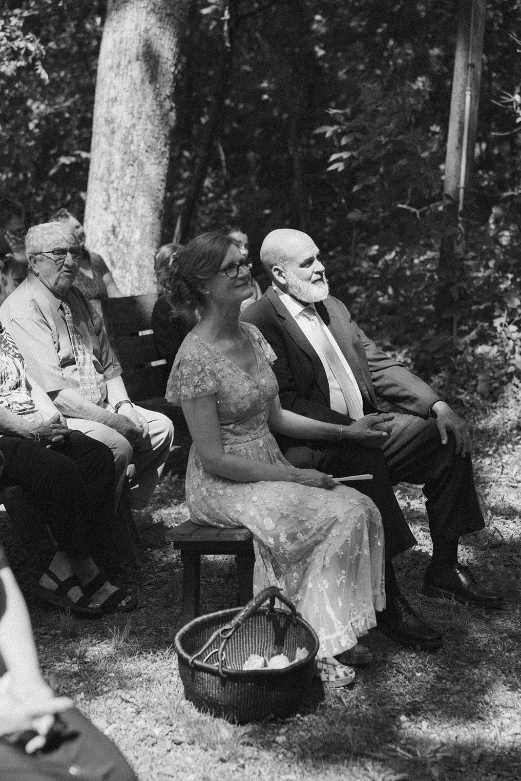 Wedding guests seated in a wooded ceremony space, surrounded by dappled sunlight at an outdoor wedding in Wisconsin.

