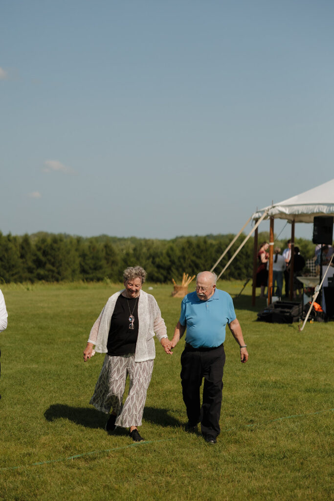 Grandparents holding hands and walking across the lawn during a joyful outdoor wedding in Wisconsin.