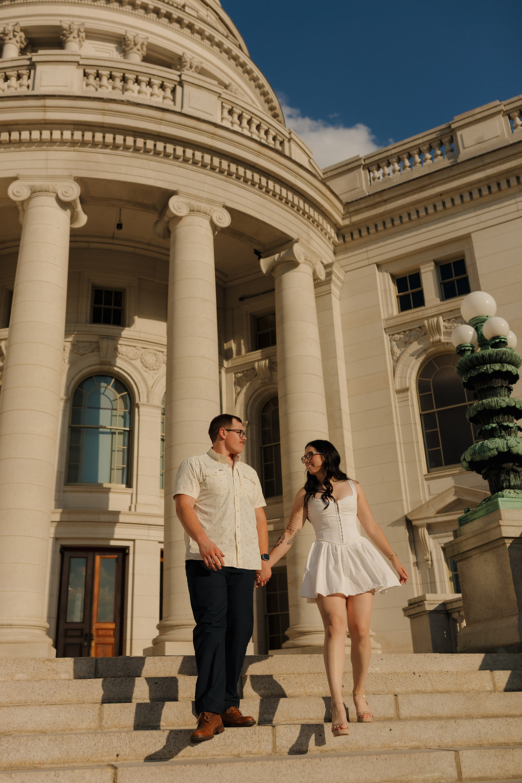 Outdoor engagement photos of a couple walking hand in hand down the Capitol steps, glowing in golden hour light.
