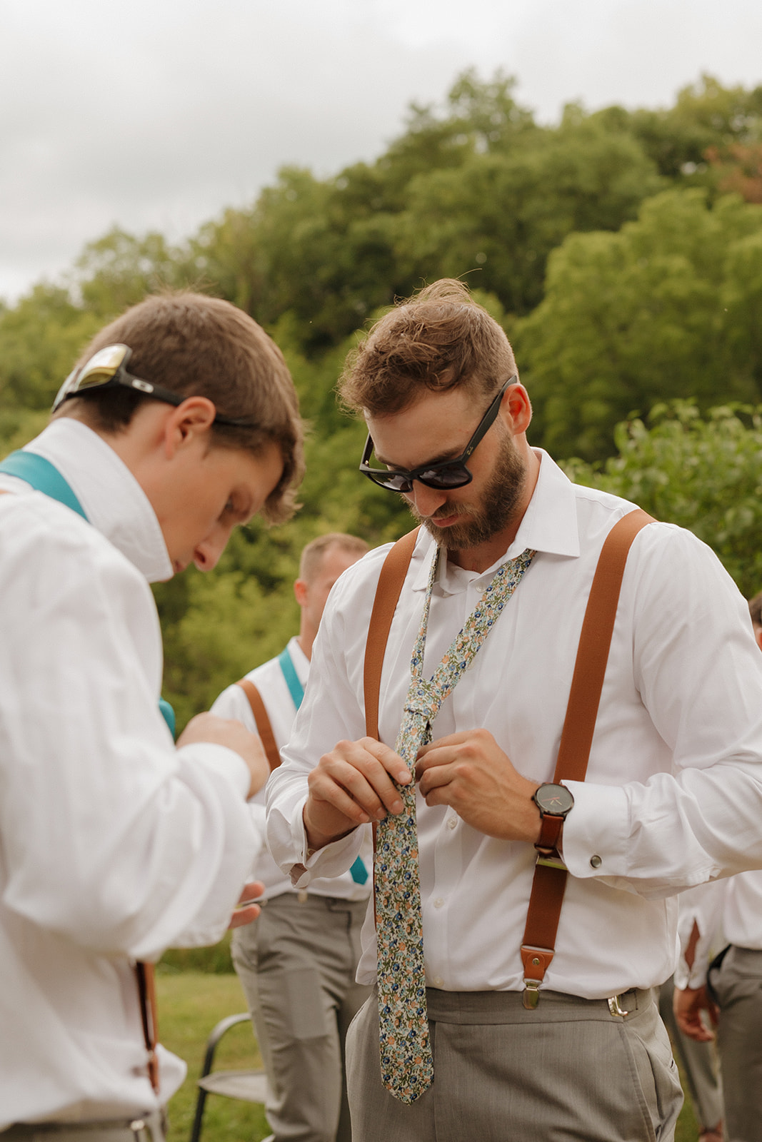 Groom getting ready with his groomsmen while tying his tie outdoors