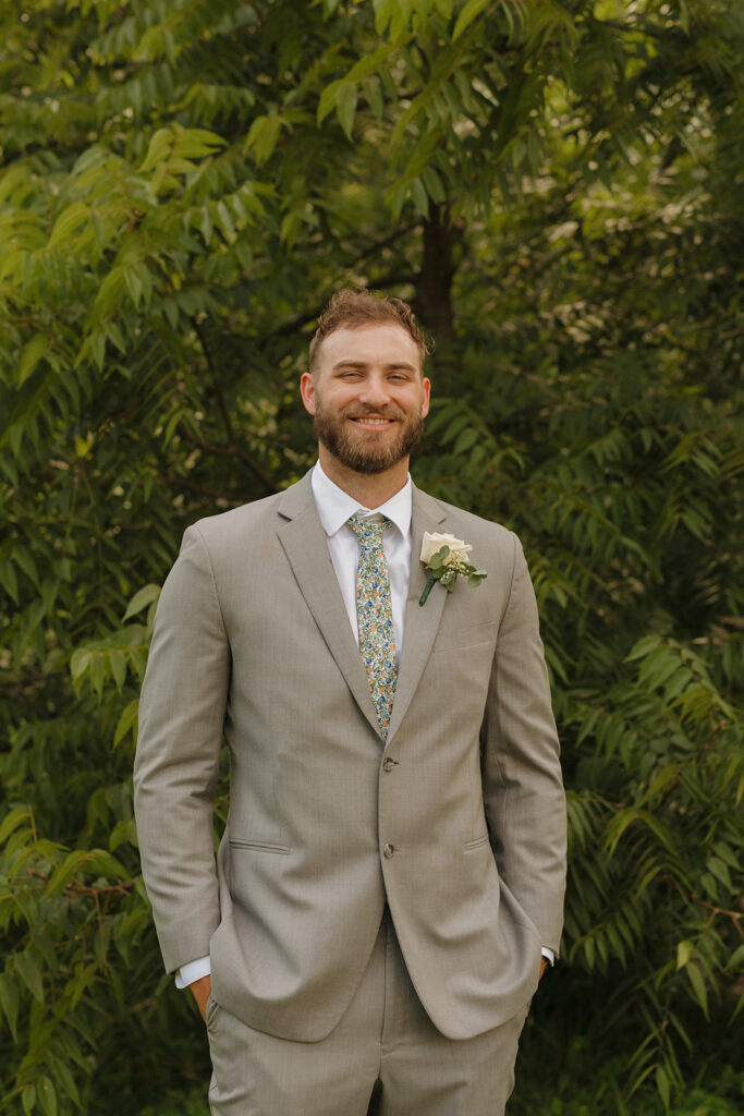 Groom wearing tan suit with hands in pockets smiles