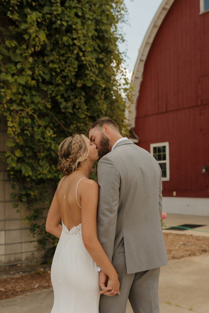 Bride and groom begin walking away while holding hands and kiss in front of red barn