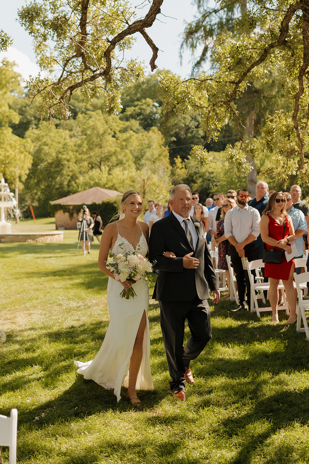 Bride being walked down aisle by her father in grassy outdoor ceremony space