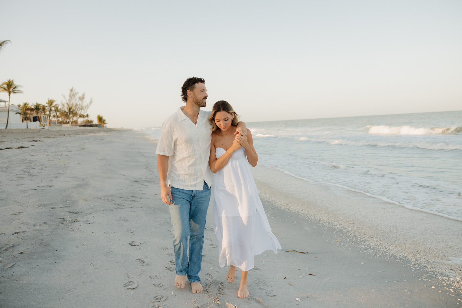 Barefoot couple walking along a quiet beach at sunset, sharing a sweet moment

