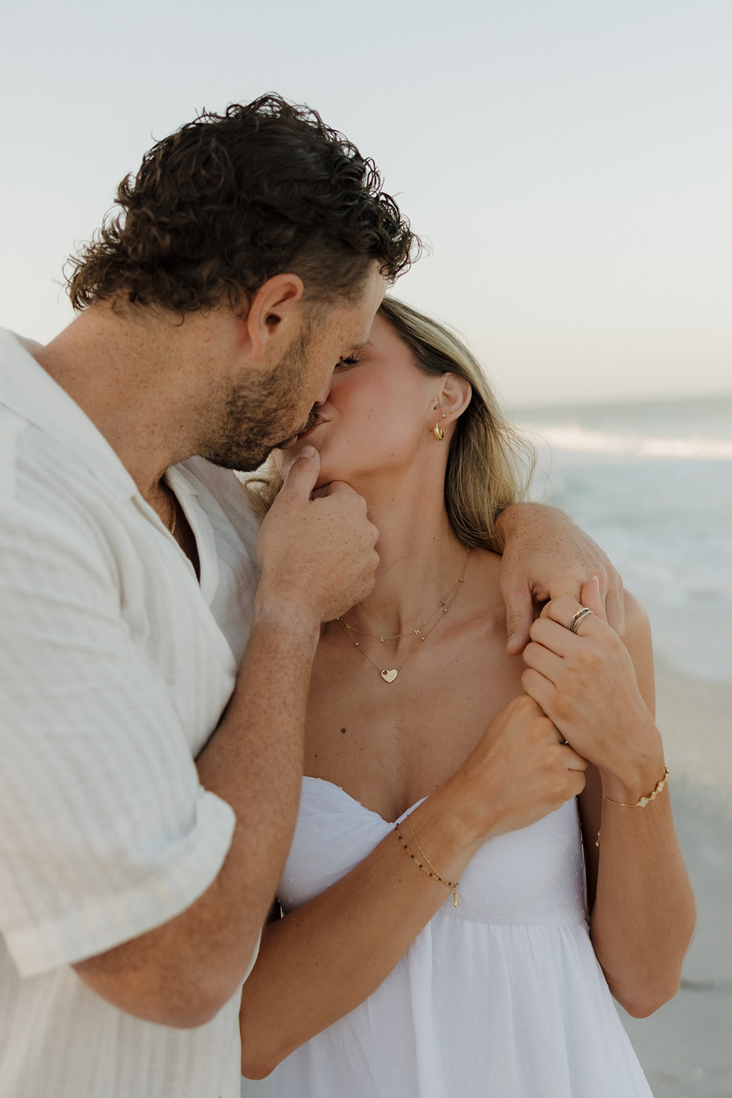 Couple kisses on beach while man holds woman's chin