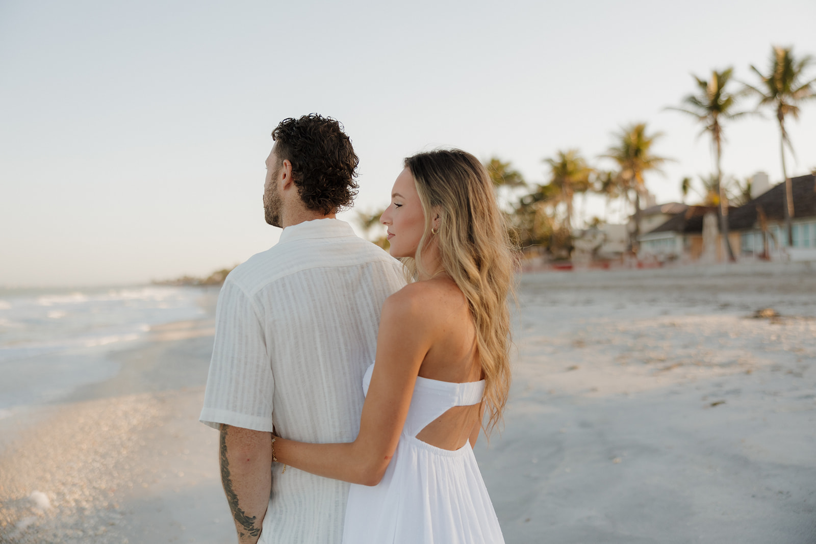 Man looks at ocean as woman stands behind him holding his waist