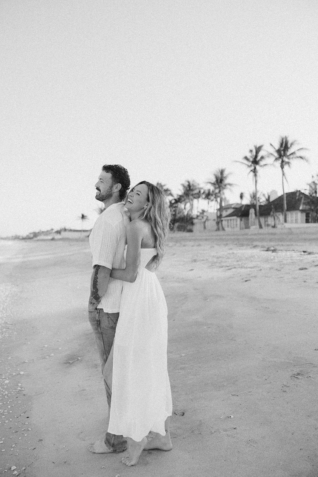 Couple laughing together while standing barefoot on the beach