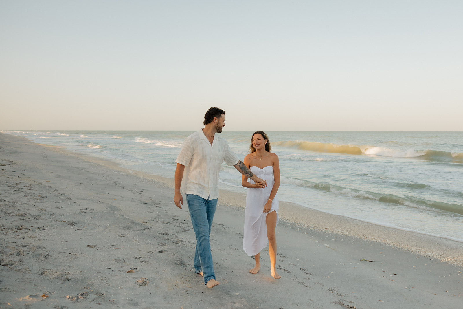 Candid shot of the couple walking hand-in-hand down a wide stretch of Florida coastline, joy all over their faces