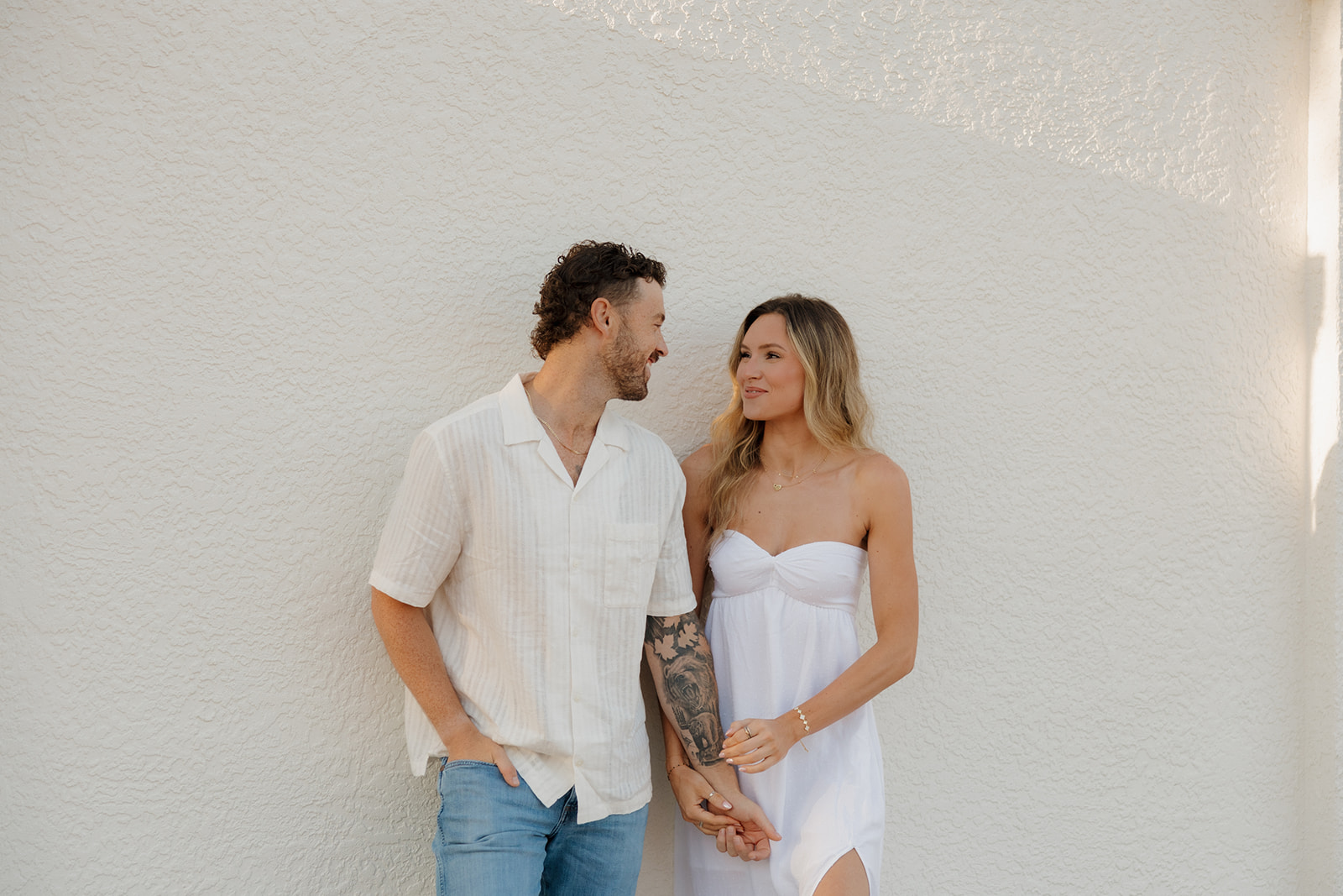 Couple holding hands while standing against white wall looking at one another after beach Florida elopement
