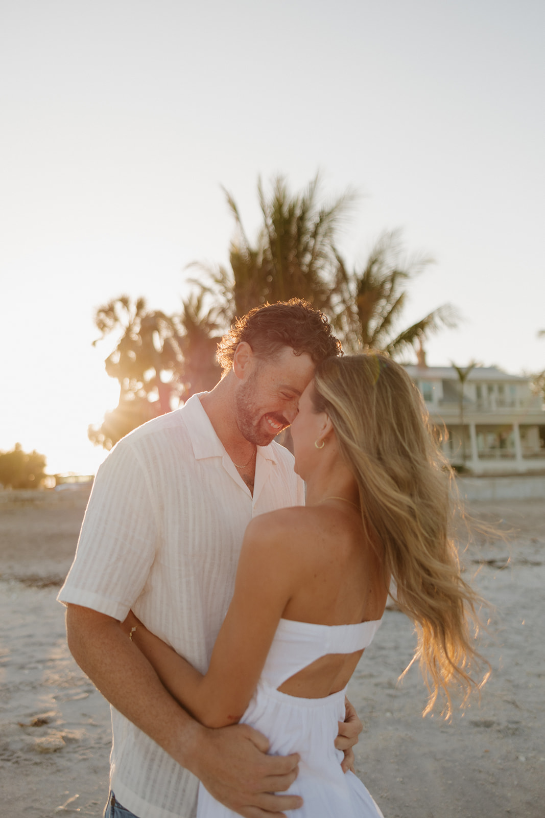 Close-up of couple laughing and embracing with golden light streaming through palm trees during their florida elopement