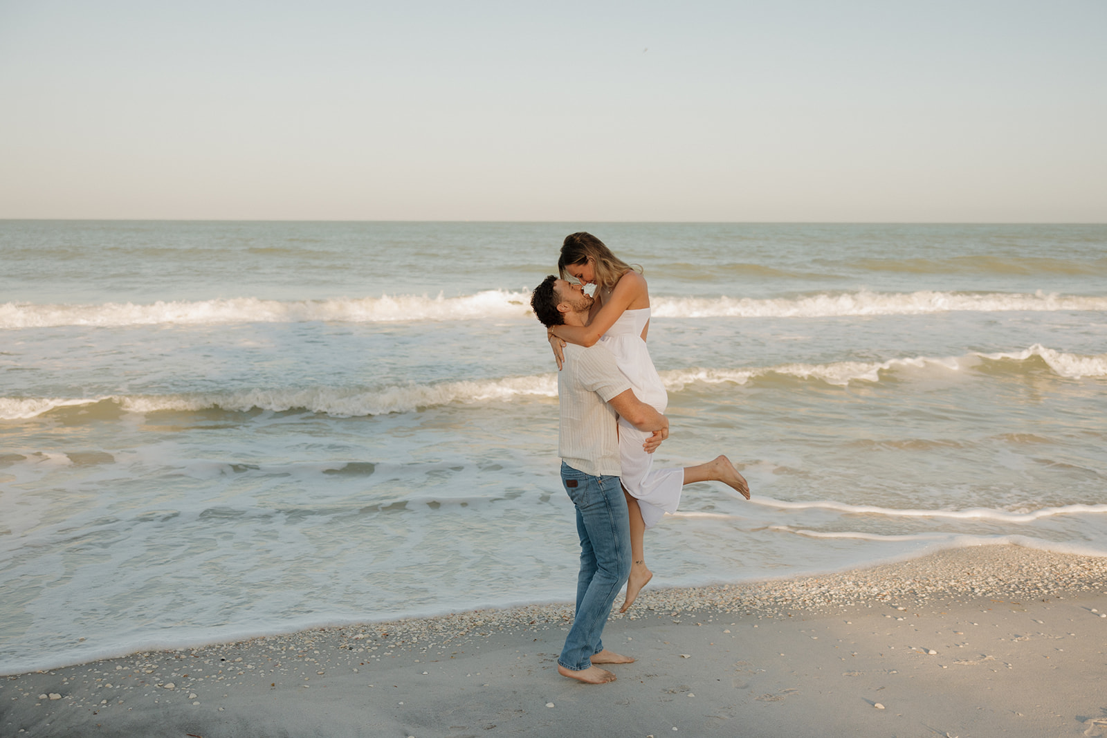 Man lifts woman in air and kisses her in front of ocean waves crashing into beach after Florida elopement