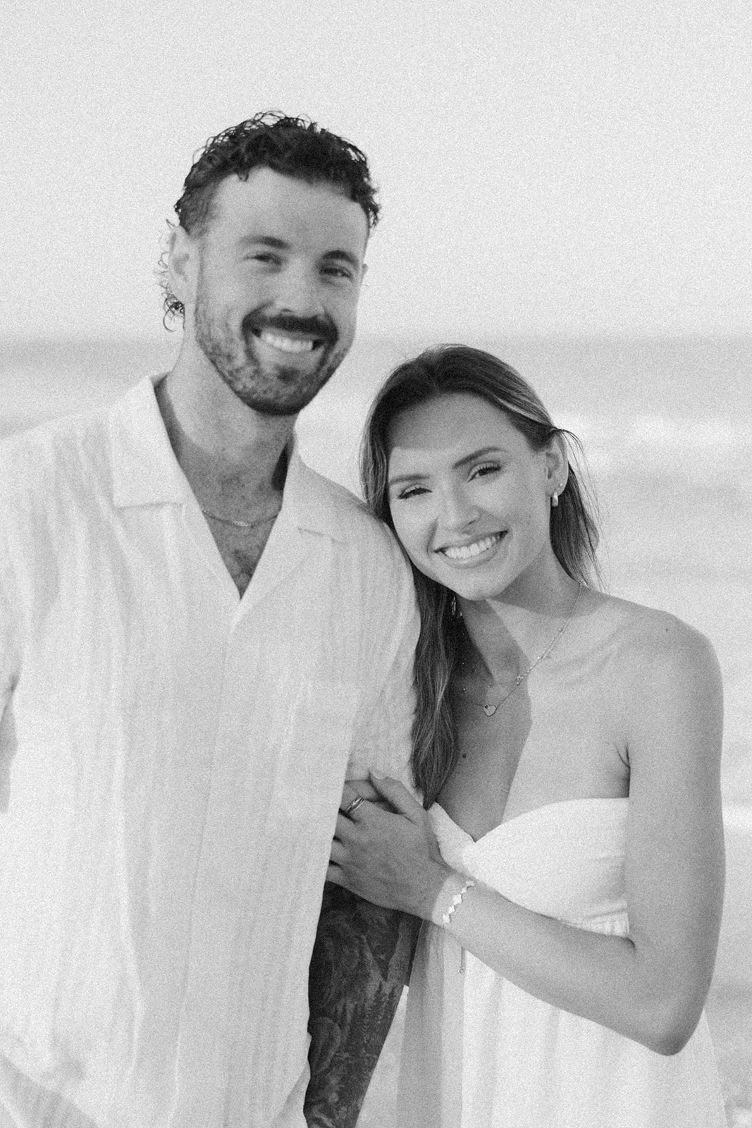 Woman holding man's arm smiling in front of ocean 