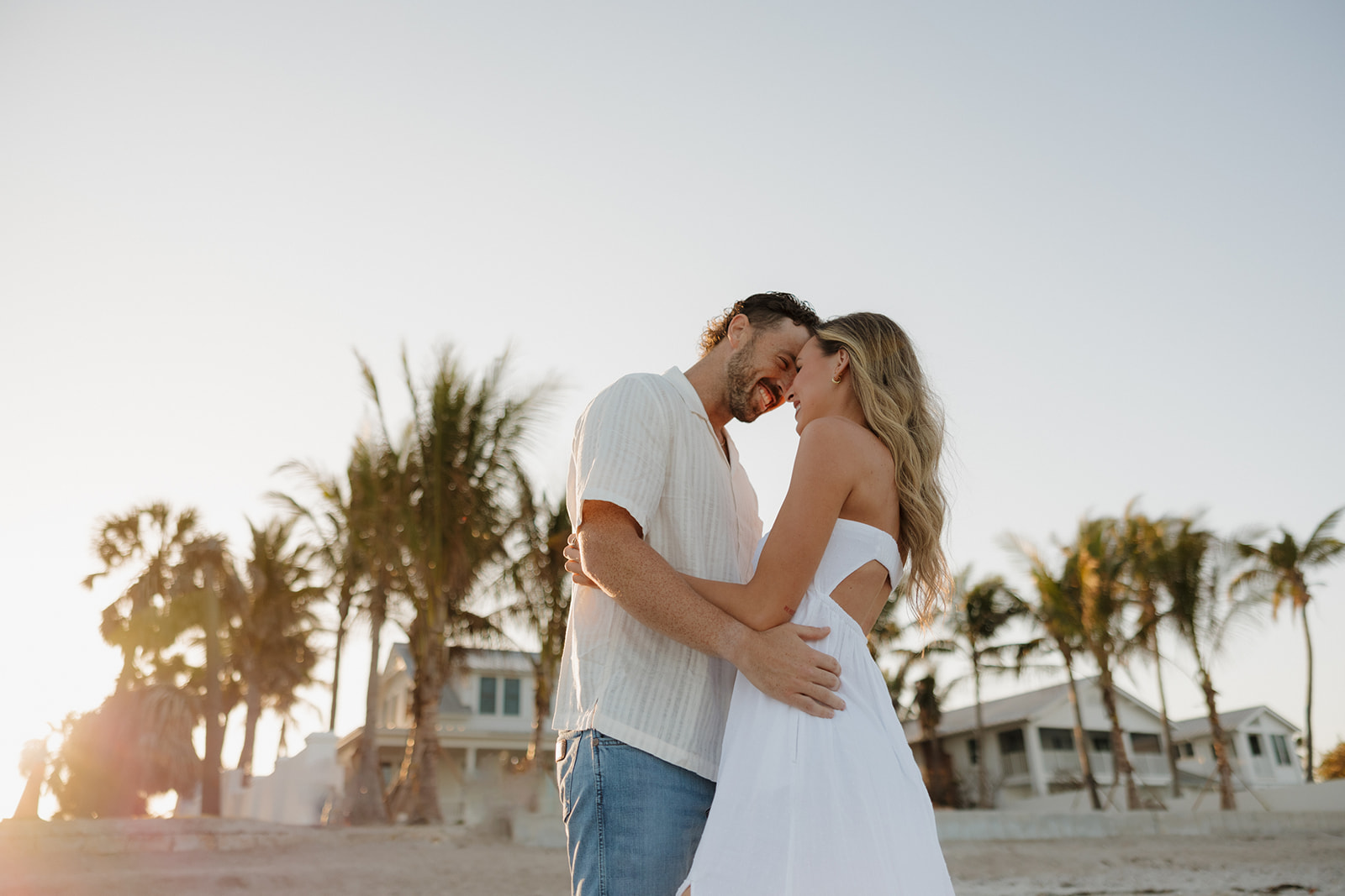 Couple pressing foreheads together while standing on the sand barefoot with palm trees beside them