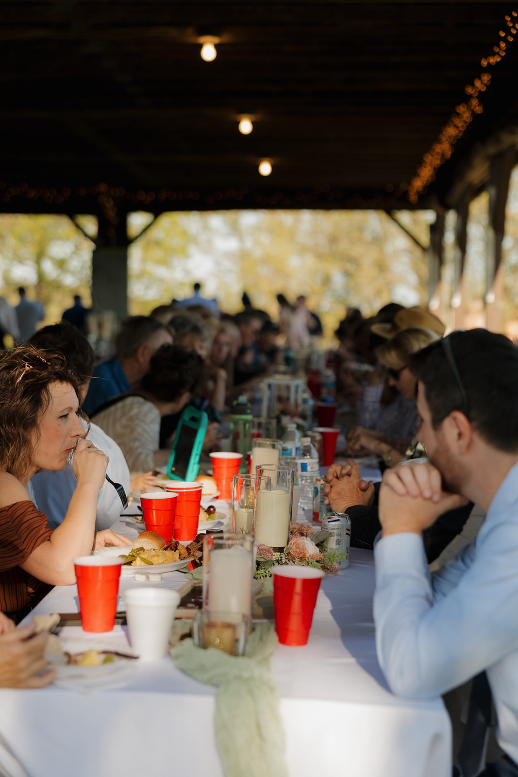 Guests gathered around a long family-style table under a rustic pavilion, enjoying dinner and conversation during an outdoor wedding reception – an inviting moment that reflects intimate wedding ideas focused on connection.