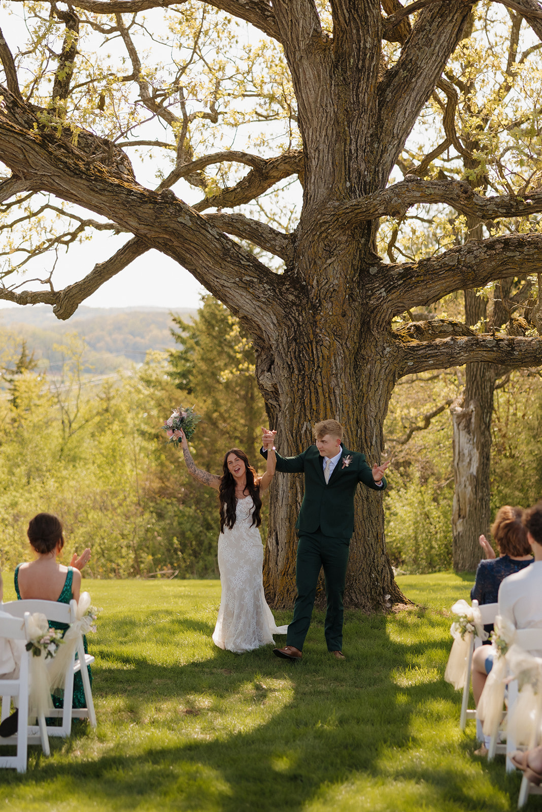 Bride and groom walk back down the aisle hand-in-hand under a giant oak tree, grinning with joy after their Madison ceremony – a radiant moment that captures intimate wedding ideas in full bloom.