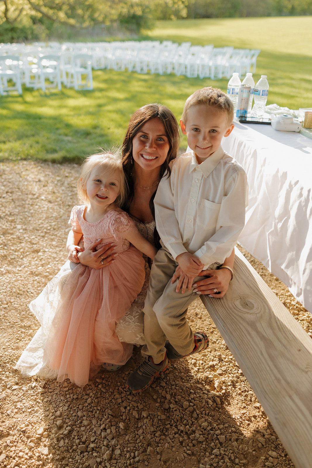 Bride kneeling and smiling with two young flower children after the ceremony, capturing a relaxed and heartfelt moment full of love and family warmth.