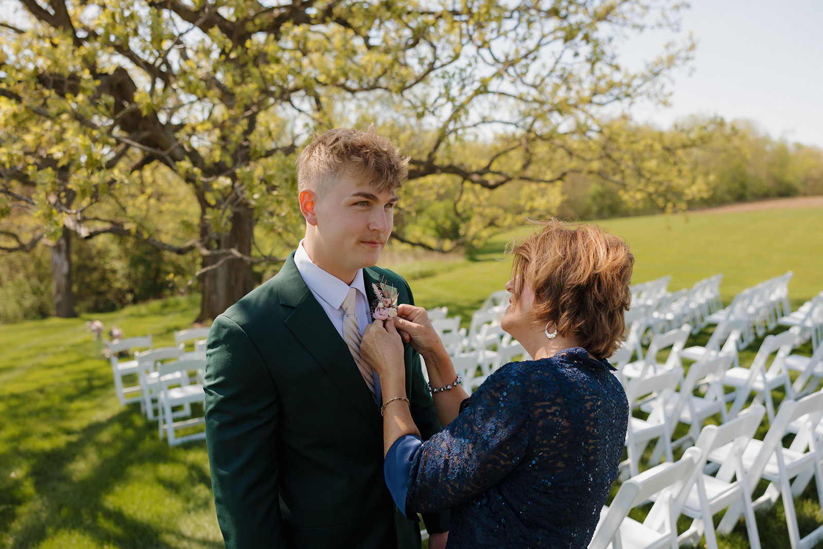 Groom’s mom pins a boutonniere on his green suit before the ceremony, sharing a quiet, tender moment in the soft morning light – one of those behind-the-scenes scenes that define intimate weddings.