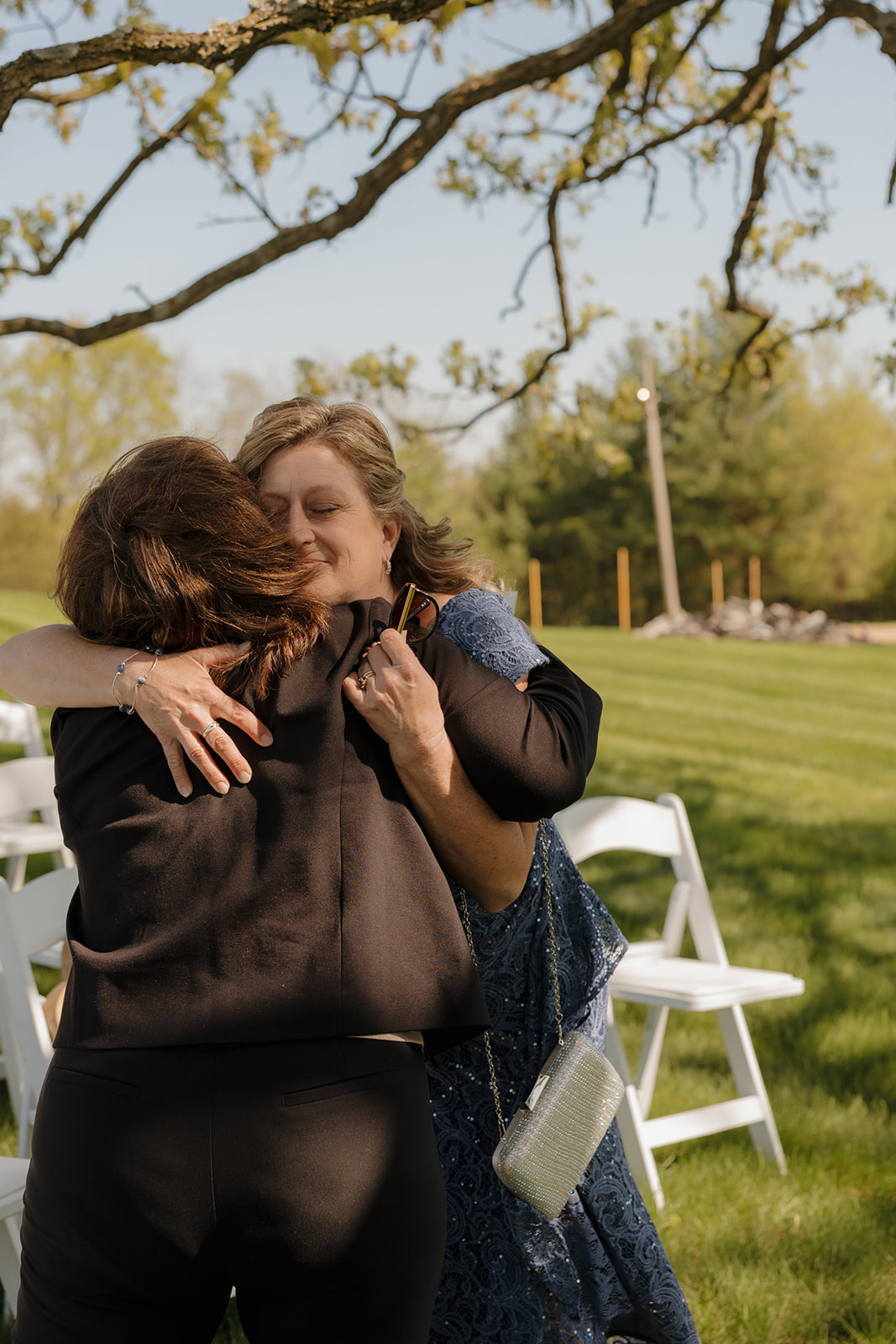 Guests embracing with emotional hugs after the ceremony under tree shade, celebrating a heartfelt wedding day surrounded by nature and love.