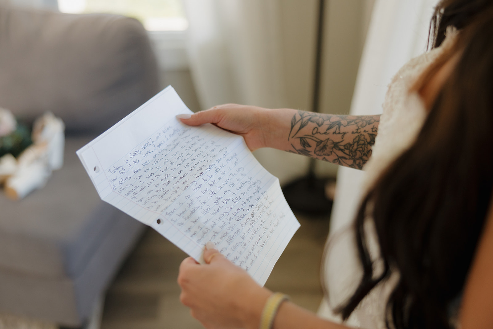 Close-up of bride holding handwritten wedding vows on lined paper, her floral tattoo visible on her arm, capturing a quiet and emotional pre-ceremony moment.