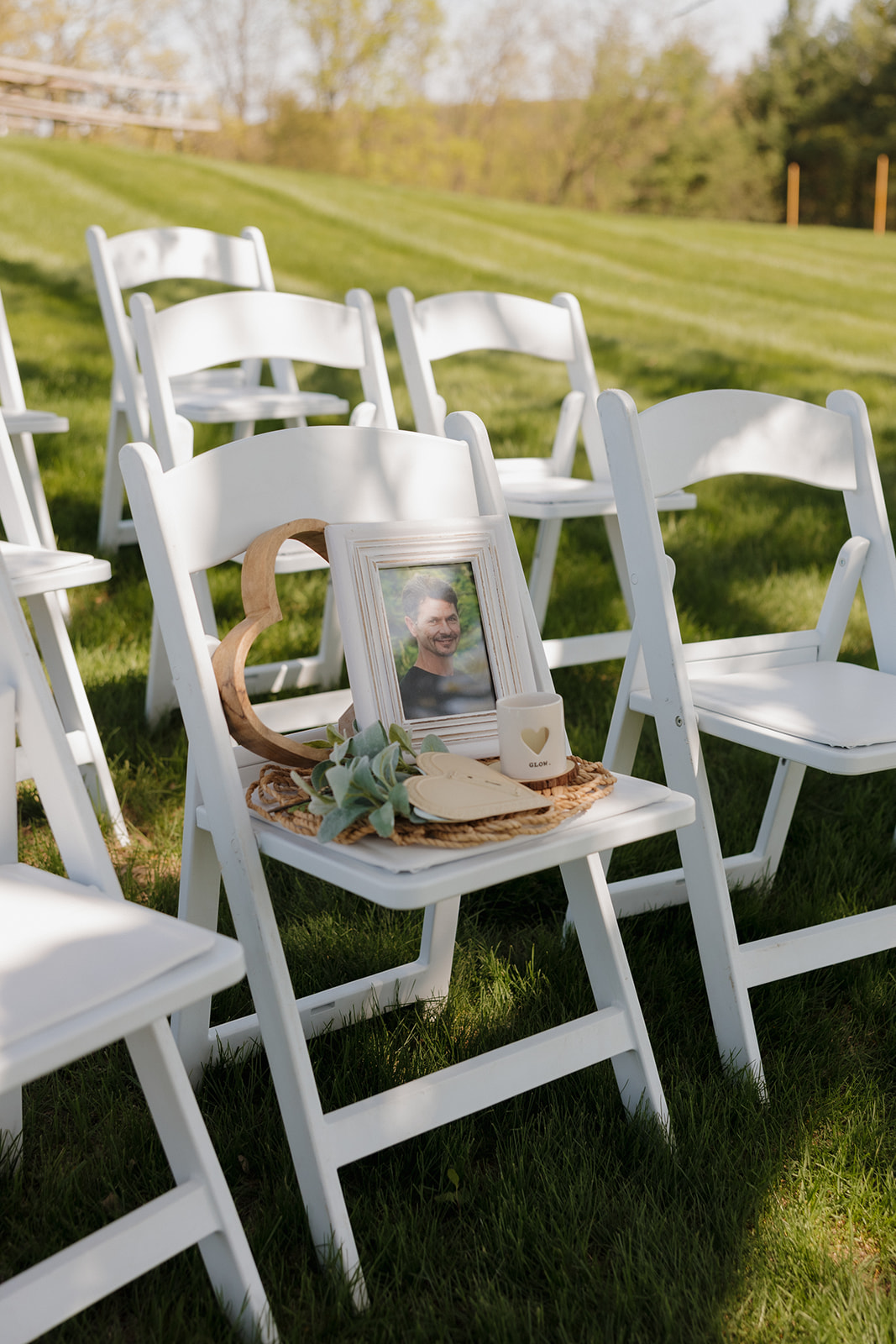 Memorial chair honoring a lost loved one with a framed photo, succulent, and candle, thoughtfully placed among guest seating during an outdoor ceremony – a heartfelt and personal touch for intimate weddings.