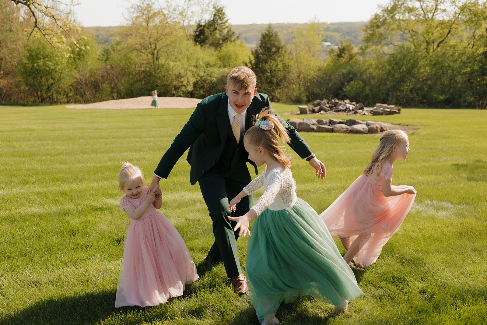 Groom playing tag with flower girls in pastel dresses during the wedding reception on a sunny Wisconsin lawn – an effortlessly playful moment inspired by intimate wedding ideas.