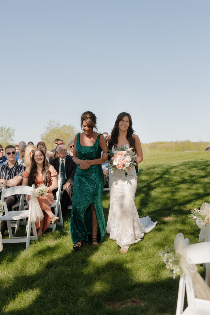 Bride walks down the aisle barefoot with her mom by her side, holding a pink bouquet and smiling radiantly – a meaningful moment full of love and a sweet example of intimate wedding ideas.