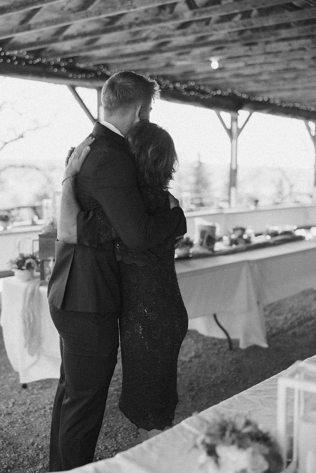 Black and white photo of groom hugging his mother tightly in a pavilion before the ceremony, capturing the deep emotion and personal connection that are central to intimate wedding ideas.