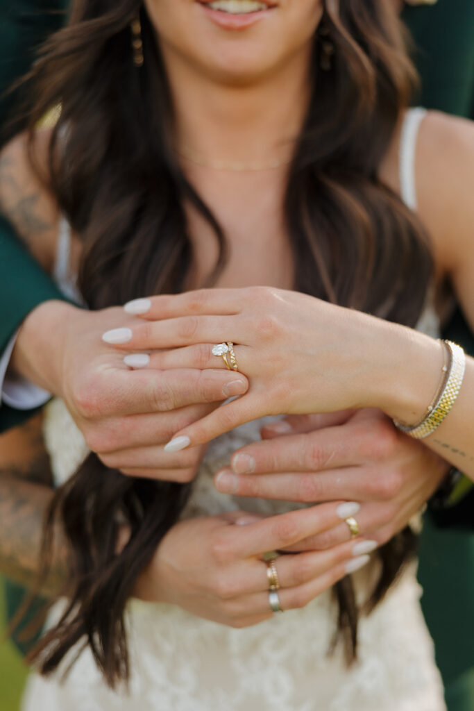 Detail shot of bride and groom’s intertwined hands, showing off their wedding bands and the bride’s pear-cut engagement ring.

