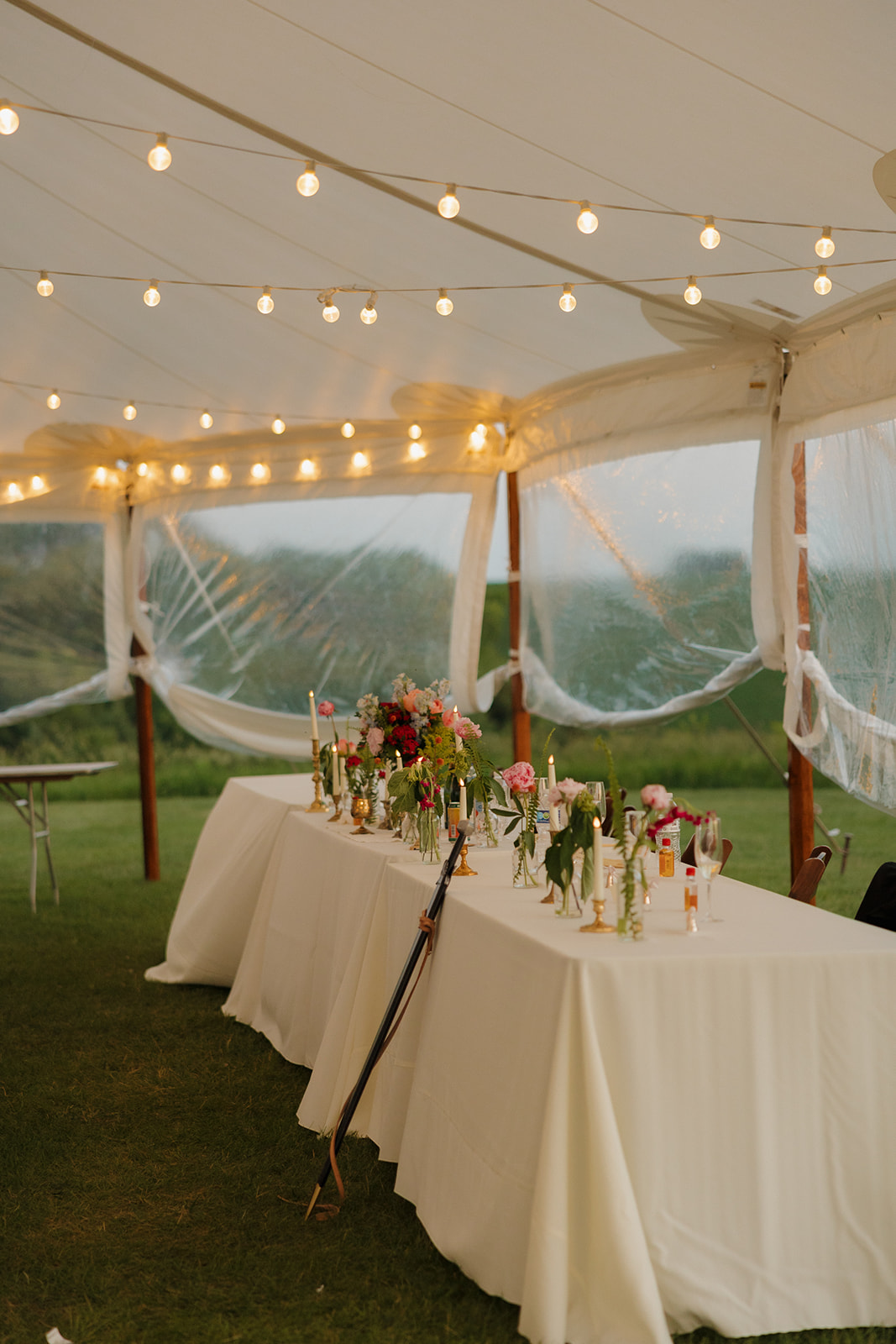 Reception head table filled with flowers and flickering candles beneath twinkly string lights as the evening sets in.

