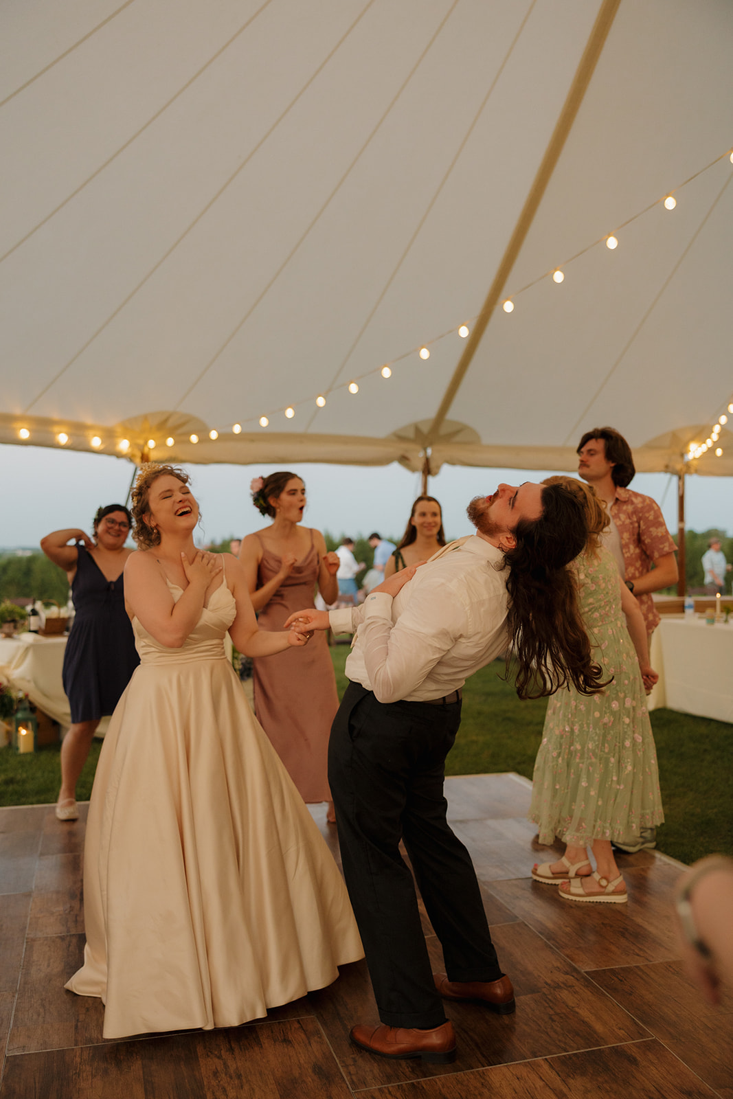Bride and groom share a carefree dance surrounded by guests and twinkle lights at their joyful outdoor wedding in Wisconsin.

