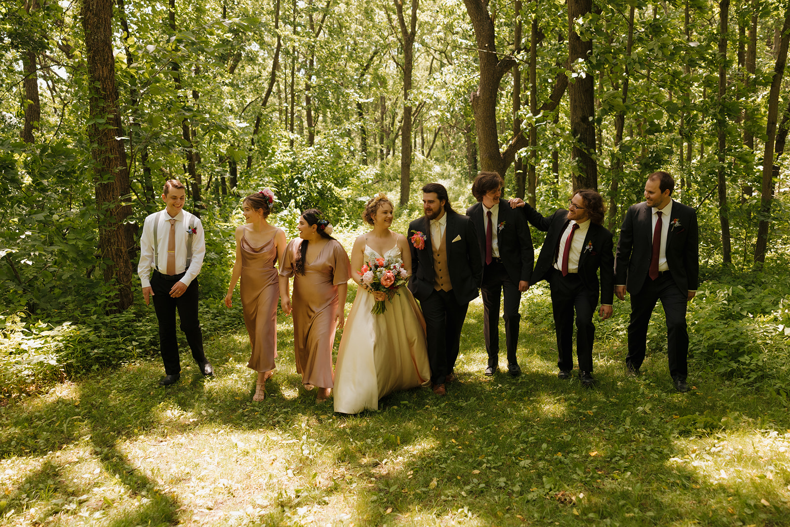 The full wedding party shares a laugh as they stroll through the forest during an outdoor wedding in Wisconsin.

