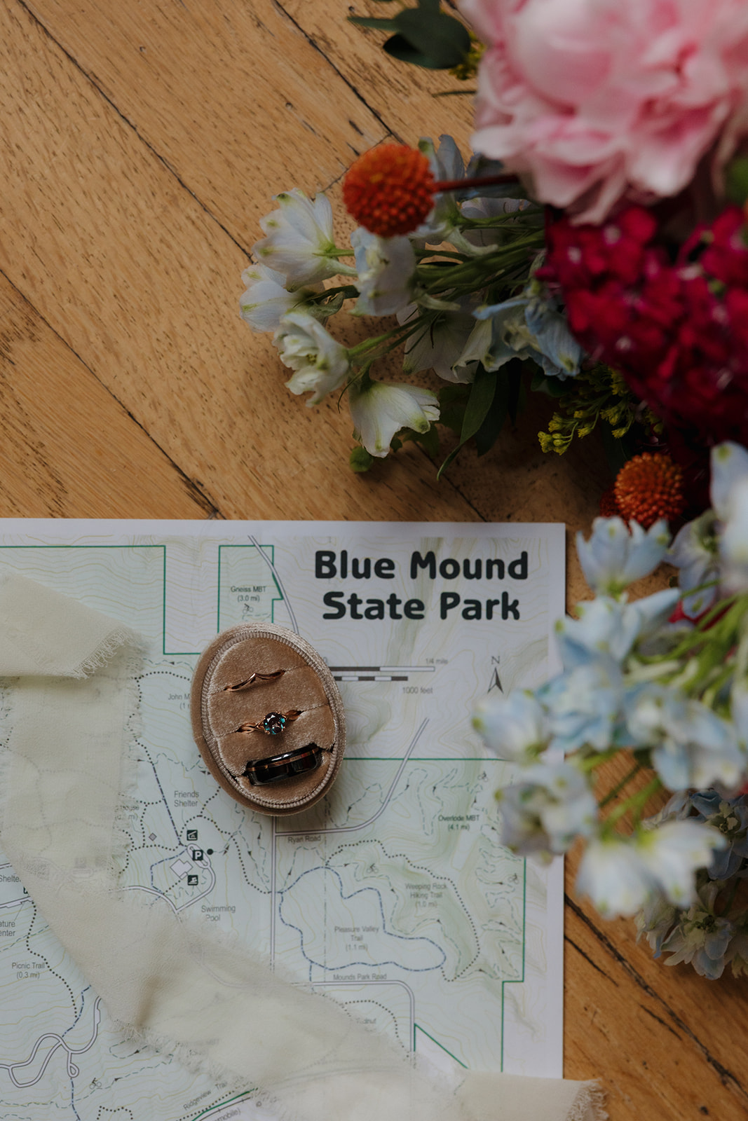 Wedding rings styled on a map of Blue Mound State Park with florals and soft fabric details—perfect for a nature-inspired outdoor wedding in Wisconsin.