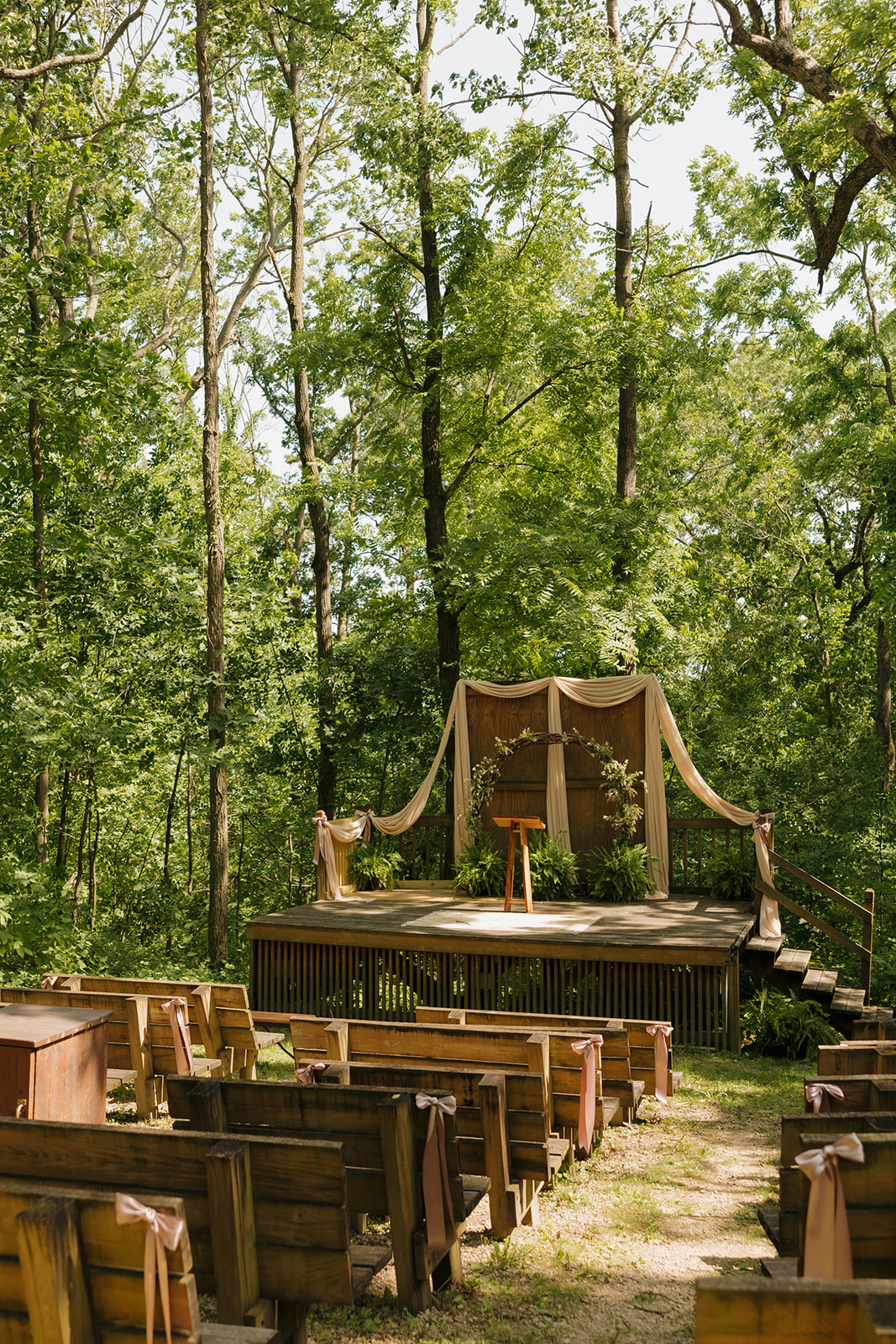 Charming outdoor ceremony site in Wisconsin with wooden benches, forest views, and a draped altar under the trees.
