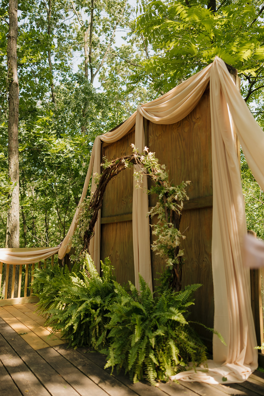 Rustic wooden wedding altar framed with greenery and blush drapery on a forest stage, ready for the vows to begin.