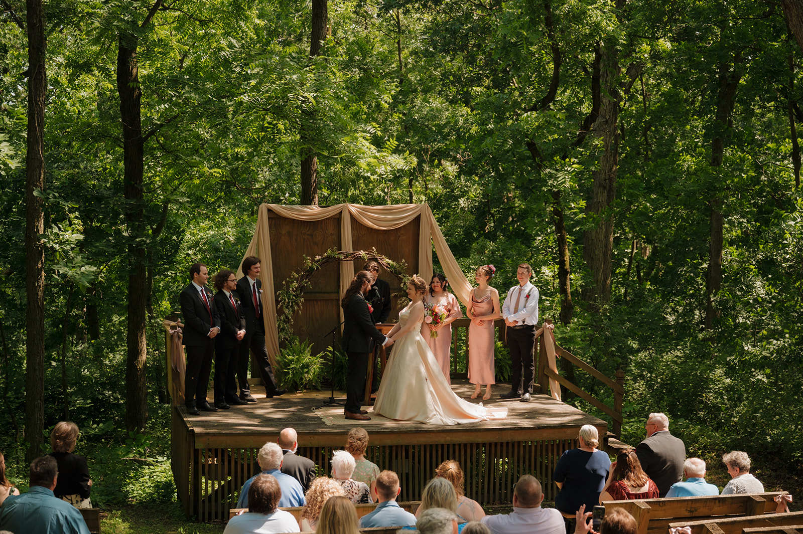 Guests watch as the couple exchanges vows on a forest stage surrounded by greenery—an unforgettable outdoor wedding in Wisconsin.

