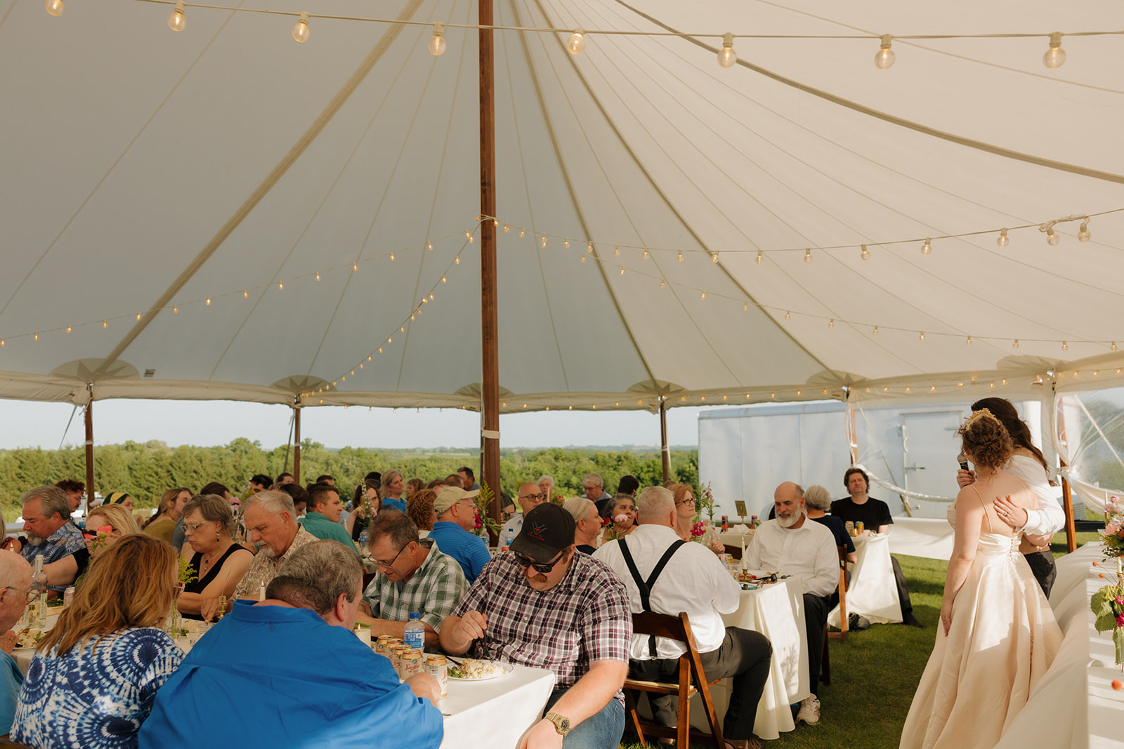 Guests enjoy a dinner reception under the sailcloth tent, surrounded by forest views and good vibes at an outdoor wedding in Wisconsin.

