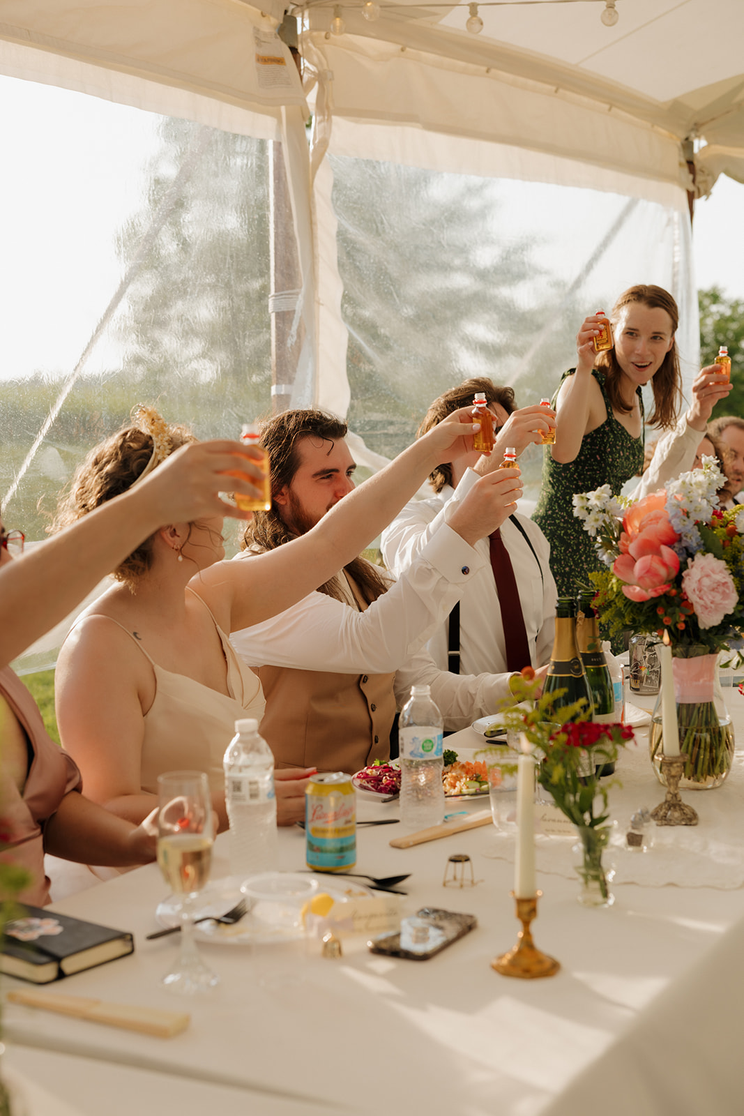 Guests raise glasses during a joyful reception toast under a clear wedding tent, celebrating love and laughter at an outdoor wedding in Wisconsin.

