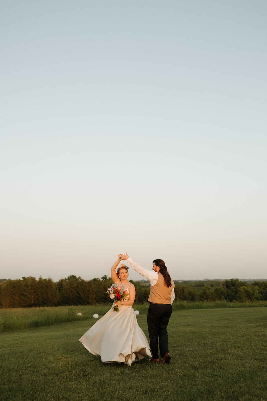 Groom spins the bride in a joyful twirl as they dance in a wide open meadow during an outdoor wedding in Wisconsin.

