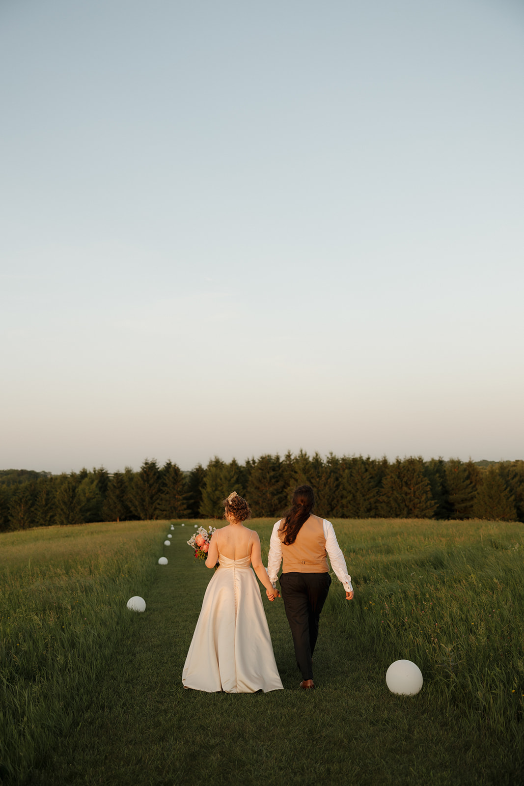 Newlyweds stroll into the sunset through a scenic meadow pathway, glowing with post-ceremony joy.

