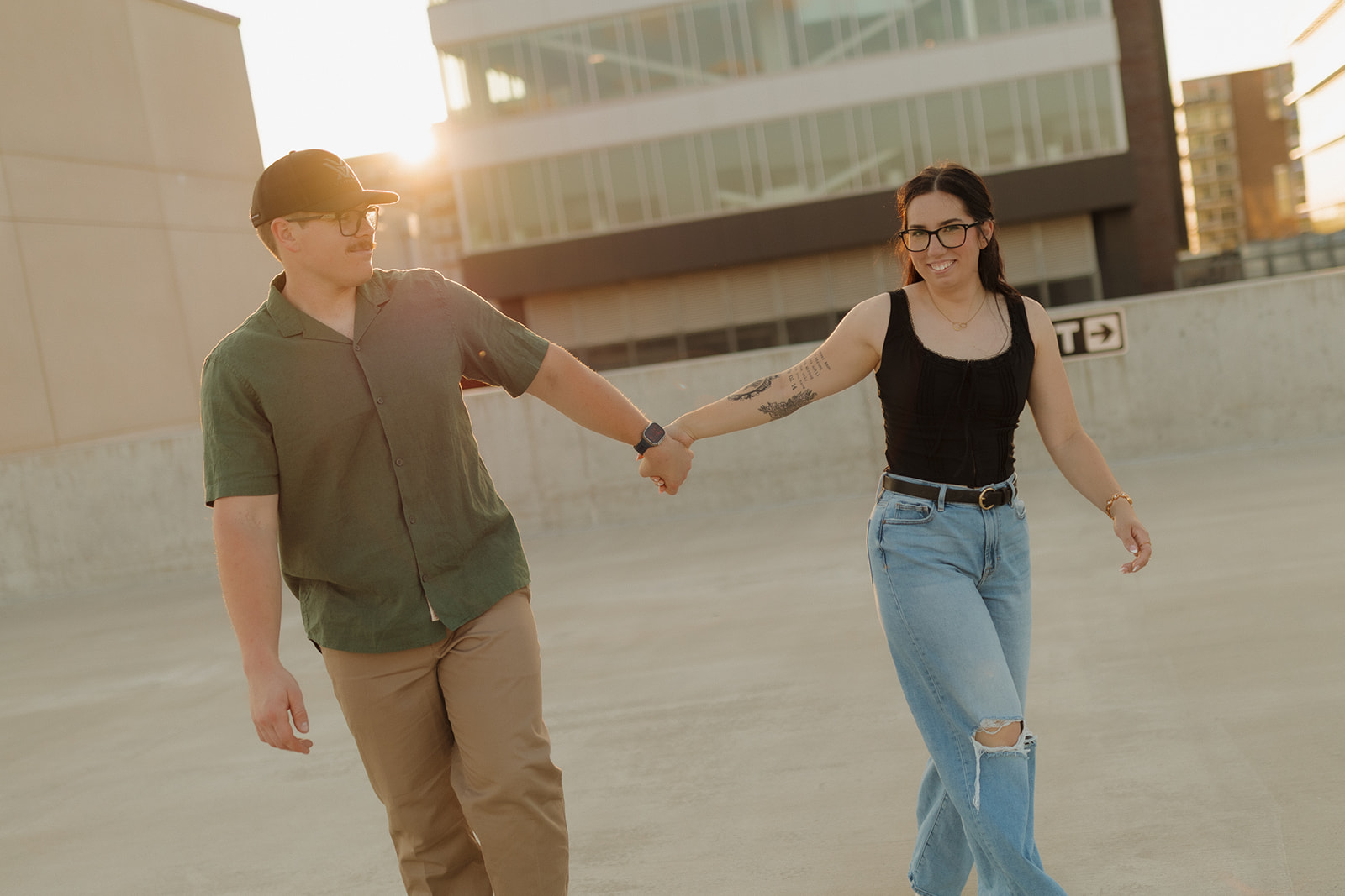 Modern couple walking hand in hand on a rooftop at golden hour, smiling and relaxed.

