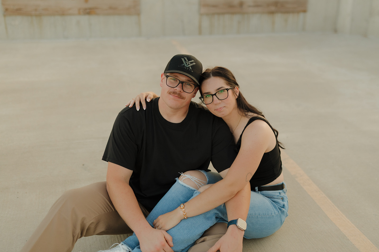 Outdoor engagement photos of a couple sitting close together on a rooftop, relaxed and softly smiling.